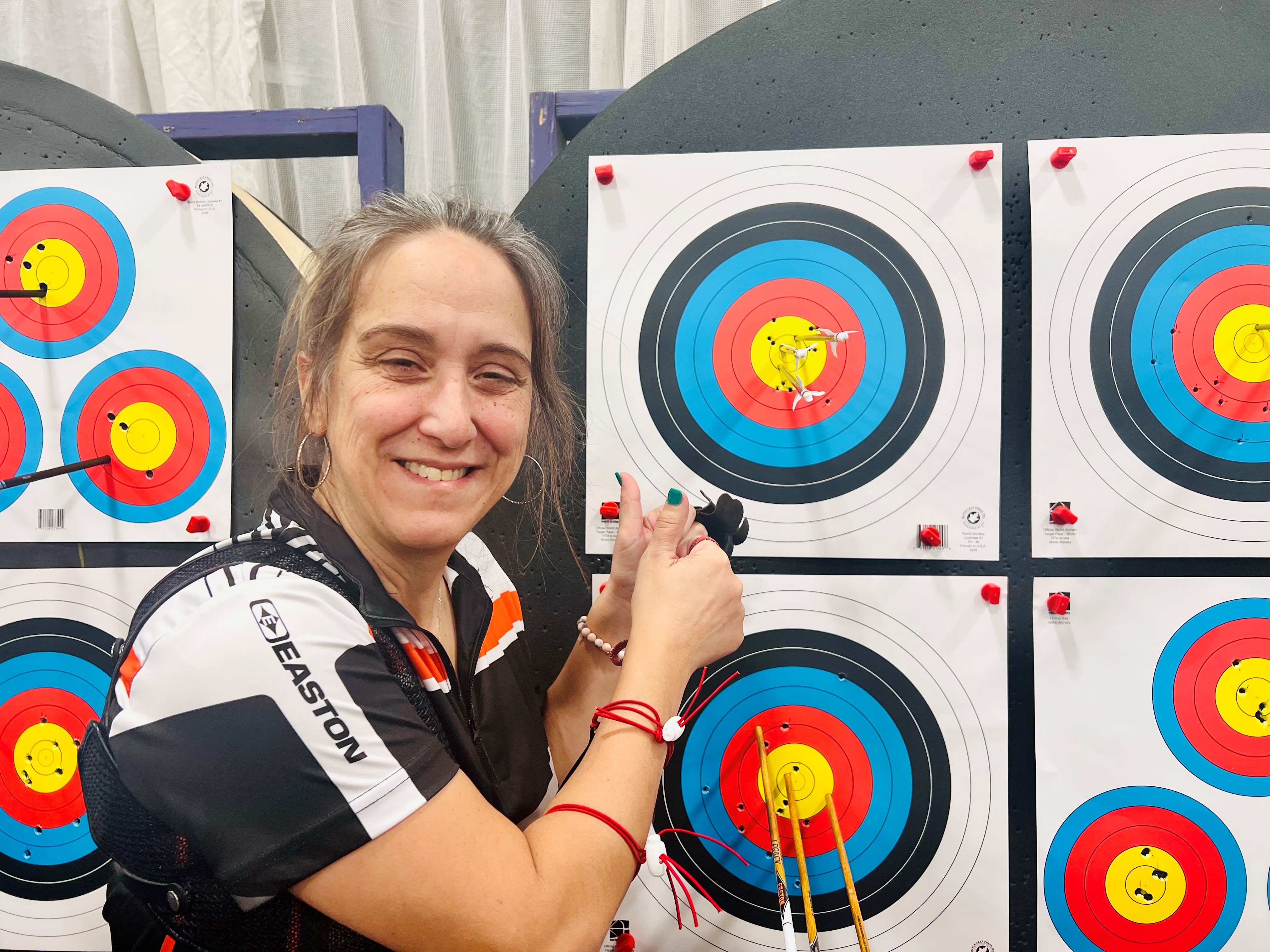 Jamie McCarrison poses in front of her target with 3 arrows in the yellow bullseye. Jamie McCarrison poses in front of her target with 3 arrows in the yellow bullseye.