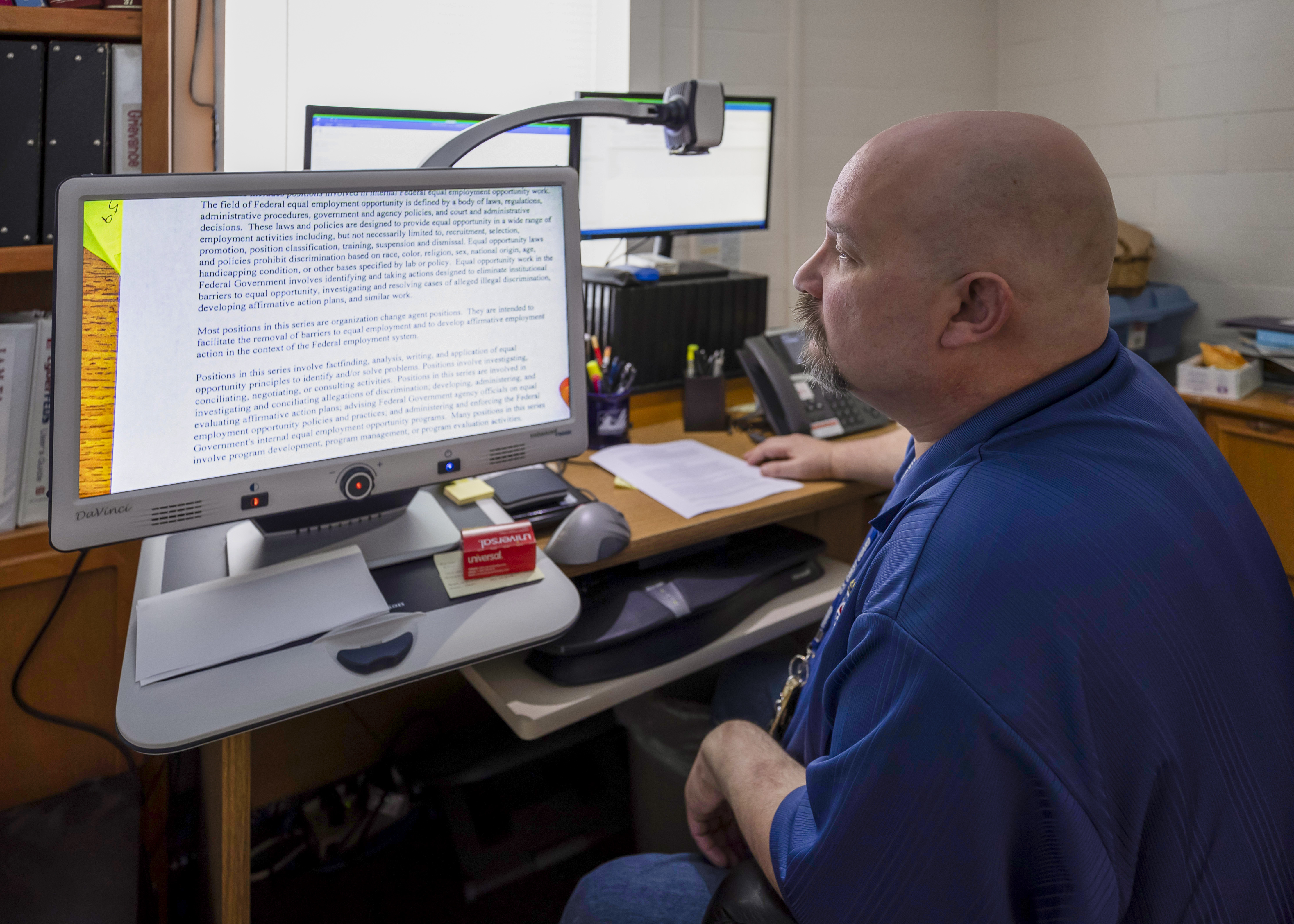 An employee is sitting at a desk with a computer with screen reader at their workspace.