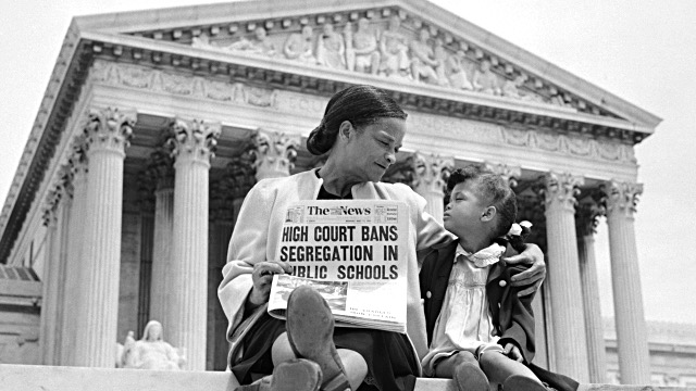 A mother and her young daughter sit on the steps of the U.S. Supreme Court. The mother is looking at her daughter while holding a newspaper with a headline that reads "High Court Banes Segregation in Public Schools."