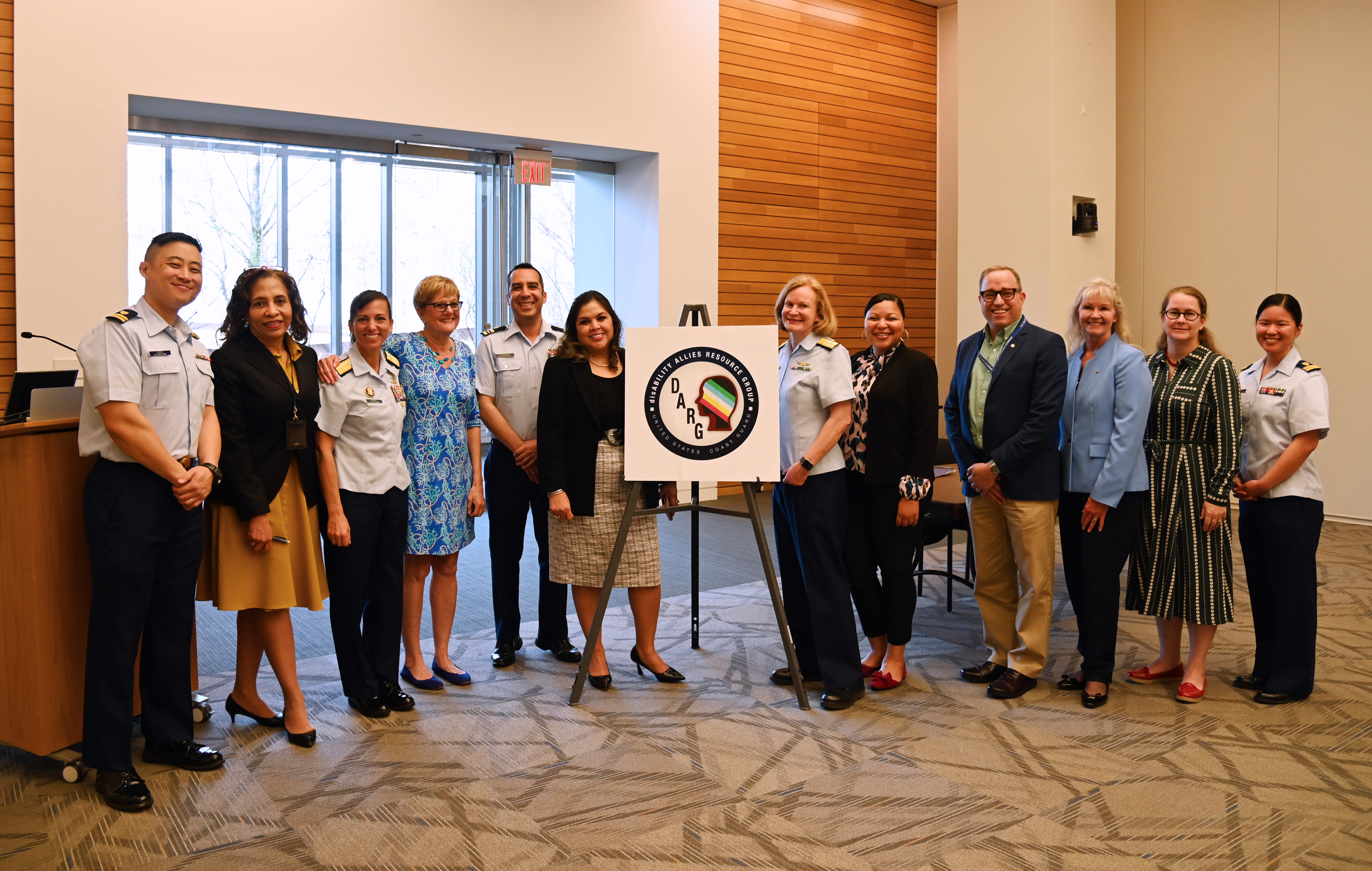 Coast Guard leadership and members of the disAbilities Allies Resource Group stand in a line posing for a group picture.