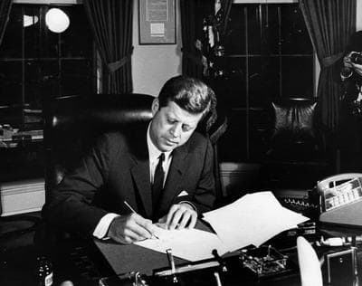 President Kennedy puts pen to paper at his desk and signs the Community Mental Health Act.